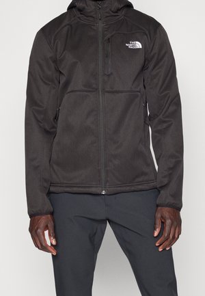 Zwarte sportjack met ritssluiting, zijzakken en capuchon. Glad materiaal met contrasterend wit logo op de linker borst.