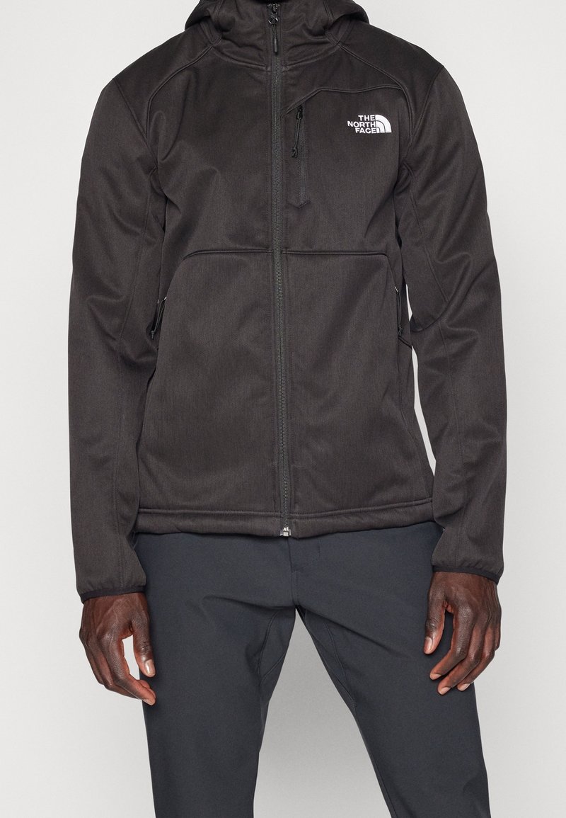 Giacca sportiva nera con chiusura a zip, tasche laterali e cappuccio. Texture liscia con logo bianco a contrasto sul petto sinistro.