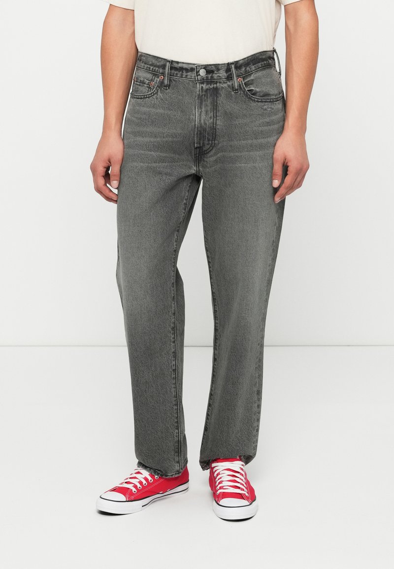 Jeans en denim gris avec une coupe droite, dotés de cinq poches, d'une fermeture à bouton et de coutures contrastées. Associés à des baskets en toile rouges.