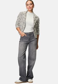 Grijze, soepel zittende denim jeans met een hoge taille, gecombineerd met een lichtgrijze coltrui en een gestructureerde zwart-witte blazer. Casual sneakers maken de look compleet.