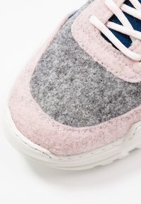 Baskets en feutre grises et roses avec une tige texturée, semelle en caoutchouc blanche et lacets rose clair. Couture notable le long des bords.