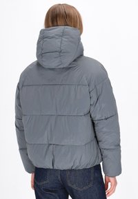 Grå polstret jakke med hætte, der har et quiltet design og elastisk nederste kant. Materialet har en glat, blank overflade.