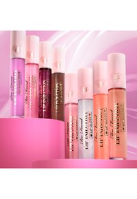 Assorted Too Faced lip glosses in various shades, featuring clear and sparkly finishes, with ribbed pastel pink caps and heart accents.