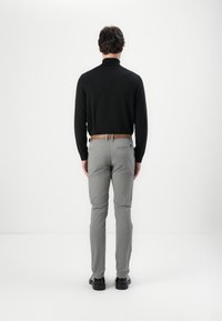 Zwarte lange mouwen top gecombineerd met lichtgrijze broek en een bruine riem, gezien vanaf de achterkant. Het materiaal lijkt glad en de schoenen zijn zwart.