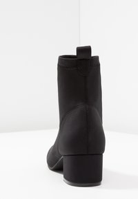 Botín negro de tobillo hecho de un textil suave. Presenta una punta redonda, tacón cuadrado y un lazo trasero para facilitar su uso. Acabado suave con detalles de costura mínimos.