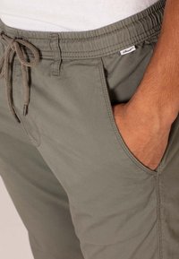 Pantalones ligeros de color verde oliva con cintura elástica y cordón. Con bolsillos laterales y una textura suave.