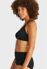 Svart spets-bh med släta kupor och justerbara axelband, kombinerad med höga spets-trosor. Båda har vågiga kanter och en texturerad design.