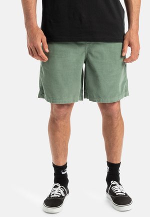 Groene corduroy shorts met een rechte snit, voorzien van zijzakken. Draag het met zwarte hoge sneakers en zwarte enkelsokken.