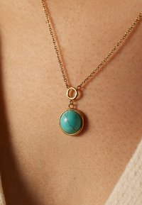Collier en or avec un pendentif circulaire en turquoise présentant des veines naturelles, suspendu à une chaîne délicate. Texture lisse et polie.