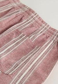 Tissu rayé rose et blanc avec une ceinture élastique et une poche plate frontale, montrant des coutures détaillées et une texture.