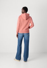 Felpa con cappuccio rosa chiaro, dal taglio casual, abbinata a jeans in denim blu a gamba larga. Cuciture a vista e design informale.