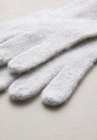 Guanti di lana grigio chiaro con una texture morbida e pelosa, con cinque dita e punte arrotondate, disposti piatti su uno sfondo neutro.