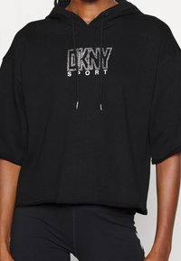 Svart kort hoodie av mjukt tyg med dragsko, prydd med "DKNY SPORT"-logotyp i rhinestones framtill.