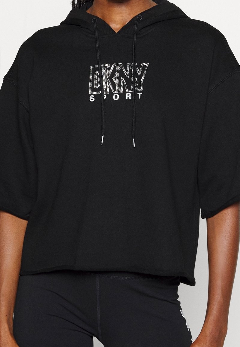 Svart kort hoodie av mjukt tyg med dragsko, prydd med "DKNY SPORT"-logotyp i rhinestones framtill.
