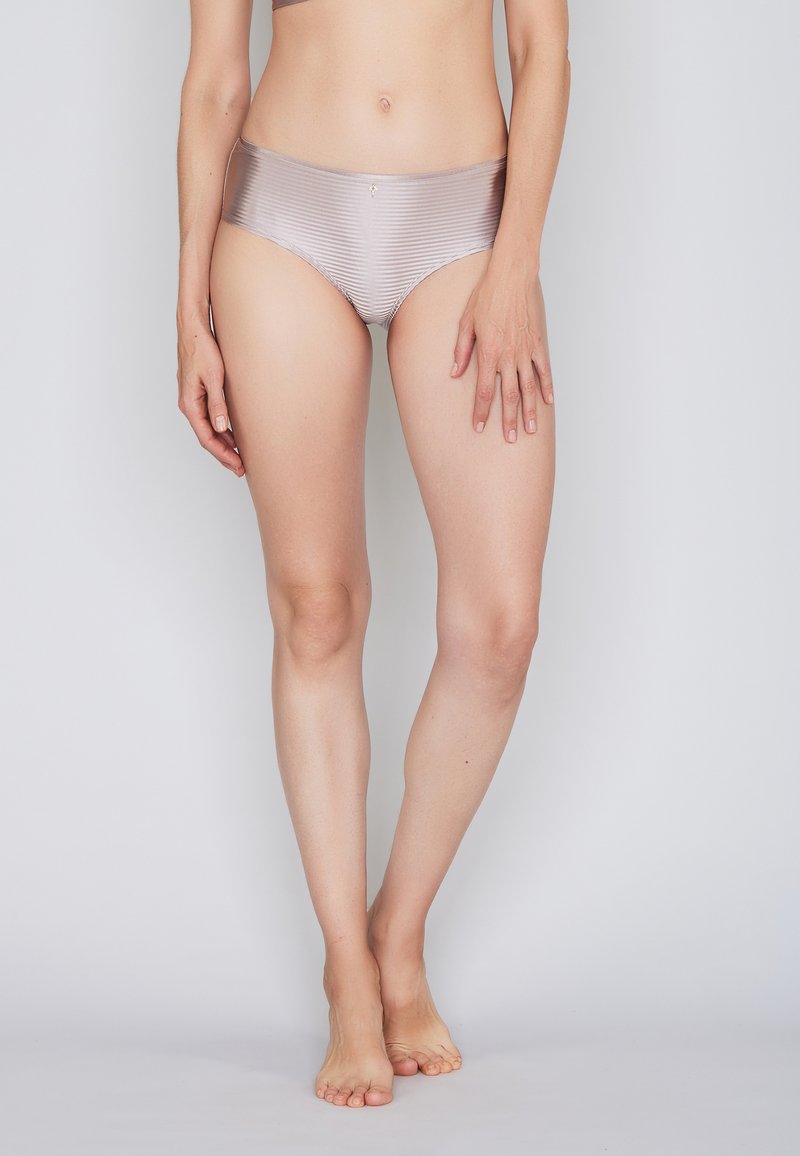 Helles beige Bikinihöschen mit glatter, glänzender Textur und dünnen Streifen. Verfügt über einen mittelhohen Schnitt und minimale Hardware-Akzente.