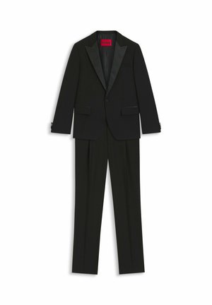 Completo smoking nero con giacca a rever in satin e pantaloni con parte frontale liscia, realizzato in tessuto morbido con una vestibilità strutturata. Etichetta interna rossa visibile.