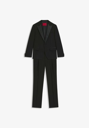 Completo smoking nero con giacca a rever in satin e pantaloni con parte frontale liscia, realizzato in tessuto morbido con una vestibilità strutturata. Etichetta interna rossa visibile.