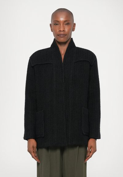 Veste en tricot noir avec une finition texturée. Les caractéristiques notables incluent un col châle, deux poches avant et une coupe ample.