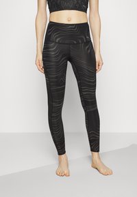 Svarta leggings med en texturerad vågig mönster, hög midja och stretchigt material, ihop med en svart croppad topp.