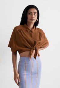 Brown cropped shirt with a button-up design and a tie detail at the waist, paired with a light blue pencil skirt featuring vertical stripes.