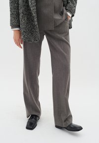 Grå herringbone ullbyxor parat med en texturerad svart-och-vit blazer, avslutat med svarta läderloafers.