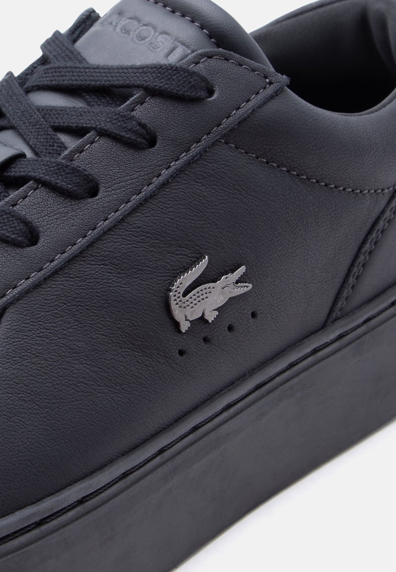 Zwart leren sneaker met zwarte veters, dikke zool en zilveren krokodillenlogo op het zijpaneel.