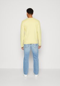 Gelbes Langarmhemd mit gerippten Bündchen, kombiniert mit hellblauen Denim-Jeans mit geradem Bein und Rücken-Taschenstickdetails.