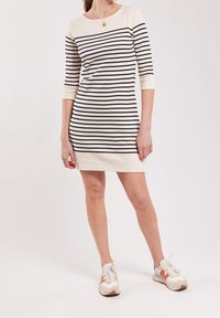 Randig klänning i krämfärg och marinblå, med trekvartsärmar och rund halsringning. Bärs med vita sneakers med orange detaljer.