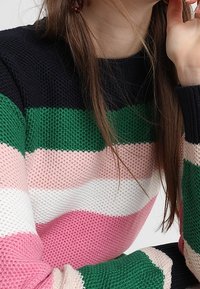 Pull en maille présentant des rayures horizontales noires, vertes, roses, blanches et des motifs texturés. Encolure ronde et manches longues.