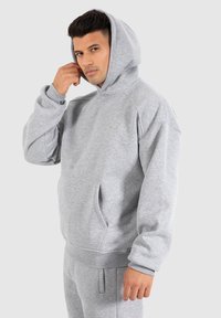 Grauer Kapuzenpullover aus weichem Material, mit einer Kängurutasche, gerippten Bündchen und einem lässigen Schnitt. Dezentes Logo-Detail auf der Brust.