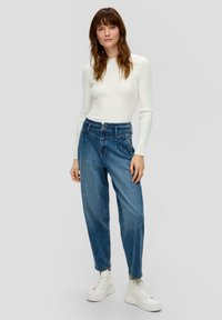 Haut à manches longues à côtes légères et jeans en denim bleu taille haute, jambe fuselée, avec des baskets plateforme blanches ; design minimaliste et texture douce.