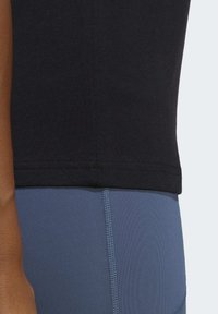 Černé bavlněné tričko s přiléhavým designem, v kombinaci s modrými legínami, které mají hladkou texturu a viditelné švy podél boku.