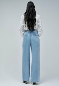 Jean large bleu clair avec taille haute et poches arrières, associé à un blouse blanche texturée à motifs floraux.