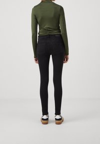 Jeans skinny de talle alto en negro con un ajuste elegante, combinados con una parte superior de manga larga ajustada en verde oliva con detalles fruncidos en la parte posterior.