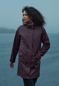 Bordeaux waterdichte jas met een hoge kraag, drukknoopsluiting en twee voorzakken. Glad, glanzend materiaal; middellange stijl.