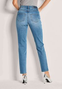  Lichtblauwe denim jeans met een hoge taille, rechte pijpen, zichtbare achterzakken en een schone afwerking. Gecombineerd met zilveren hakken.