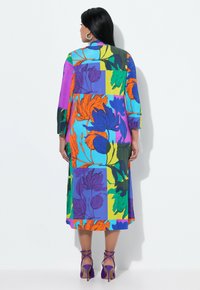 Värikäs, kuviollinen mekko, jossa on suuret kukkakuviot sinisessä, violetissa, oranssissa ja vihreässä; puolisynnykseen asti yltävä ja kolmivartiset hihat.