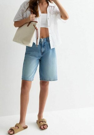 White eyelet shirt, cropped top, light blue denim bermuda shorts, brown slide sandals with buckle, and a beige tote bag with brown accents.