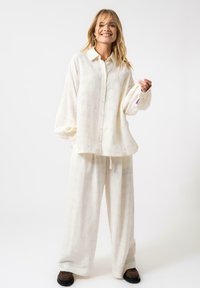 Insieme di lino leggero color crema composto da una camicia con bottoni a motivo testurizzato e pantaloni a gamba larga. Vestibilità casual con vita elasticizzata.