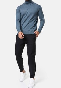 Pull col roulé bleu au design ajusté, associé à un pantalon noir fuselé et des baskets blanches. Le tissu semble doux et texturé.
