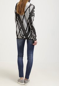 Sweter z przędzy z czarno-szarymi geometrycznymi wzorami, w zestawie z ciemnoniebieskimi wąskimi dżinsami i szarymi butami wsuwanymi.