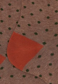 Calze a maglia marroni con pois verde scuro e sezioni del tallone di un brillante arancione, mostrate da vicino e sovrapposte.