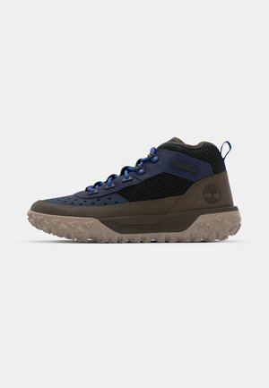 Bota de senderismo alta con parte superior sintética en azul y verde oscuro, paneles de malla, suela de goma oscura con tacos de tracción y detalle de logo.