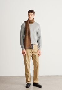 Pulover gri texturat, eșarfă maro, pantaloni bej, pantofi negri. Design simplu și culori neutre. Accent pe materialele hainelor și croială.