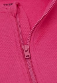 Fuchsiový zipový oděv, který má hladký zipový pás a ribovanou strukturu podél okrajů. Tkanina vypadá měkce a pružně.