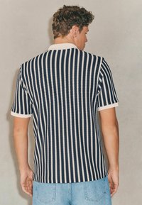 Polo din tricot cu dungi bleumarin și alb, cu mâneci scurte și guler ribat. Cu hem drept și croială lejeră, afișează un model texturat.