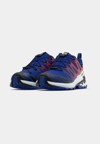 Kék és piros színátmenetes terepfutó cipő kecses kialakítással, hálós felsőrésszel, fekete kiegészítőkkel, masszív talppal és gyorsfűzős rendszerrel.