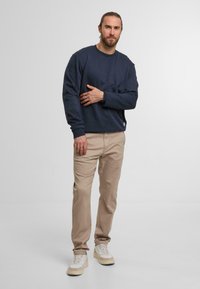Sweatshirt navy à col rond, pantalon beige et baskets claires. Le sweatshirt a une coupe décontractée et des poignets côtelés.