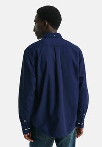 Camicia bottonata blu navy in cotone, con yoke posteriore, maniche lunghe e orlo arrotondato. Bottoni bianchi decorano i polsini e il colletto.