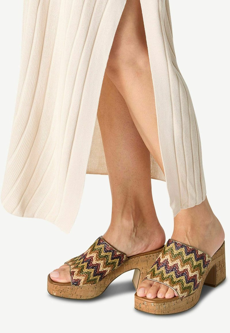 Sandales en liège avec une sangle tissée en zigzag multicolore, design à bout ouvert et talon épais, sur fond de tissu clair.